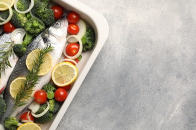 Photo of Raw fish with vegetables and lemon in baking dish on grey textured table, top view. Space for text