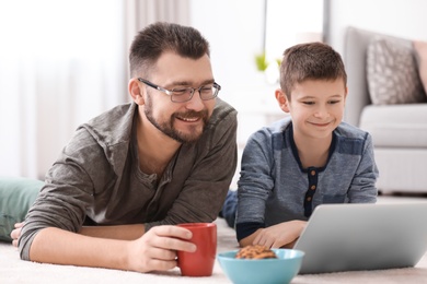 Photo of Little boy and his dad using laptop at home