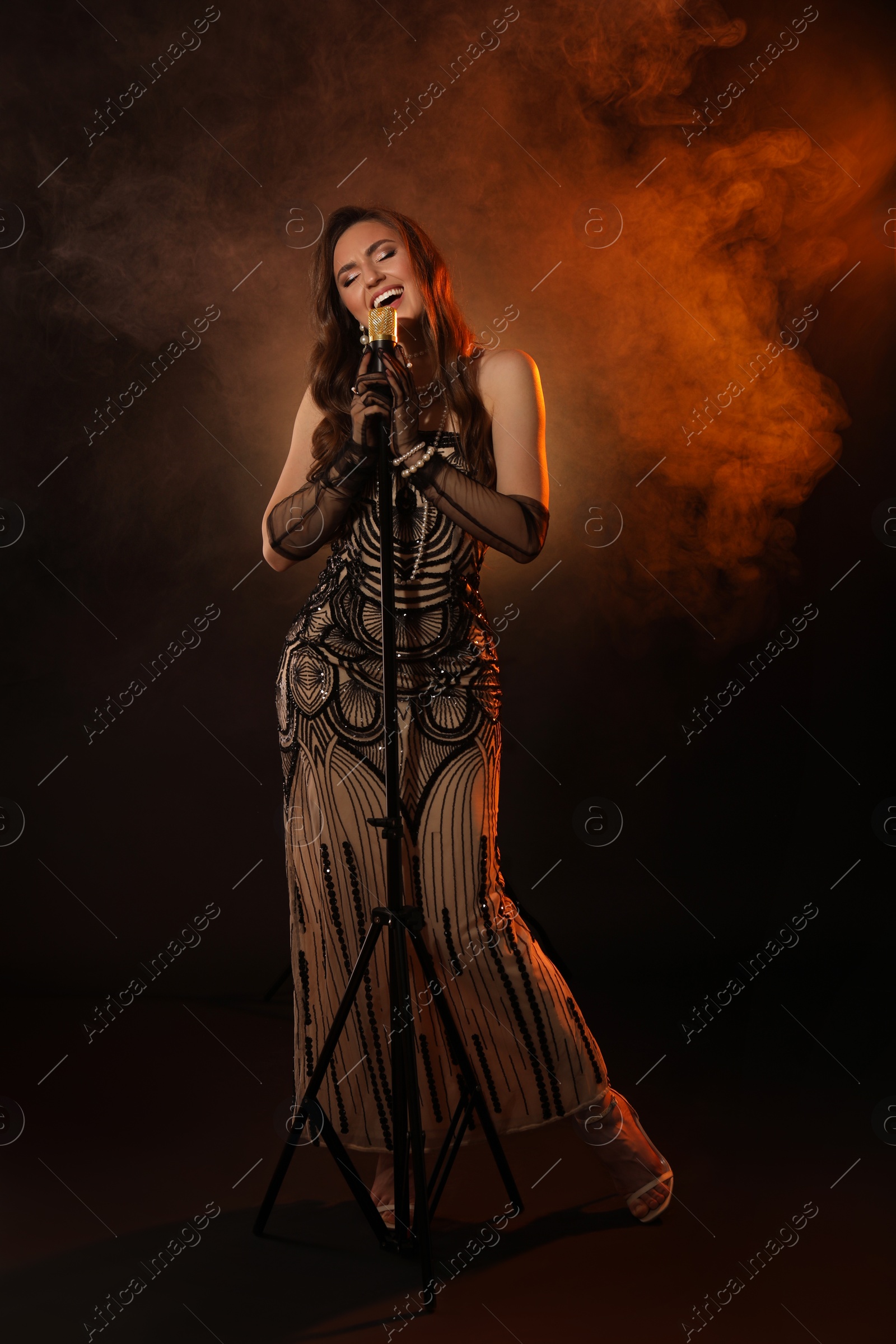 Photo of Beautiful young woman with microphone singing in color lights and smoke