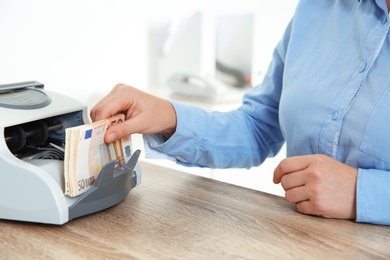 Photo of Female teller putting money into currency counting machine at cash department, closeup