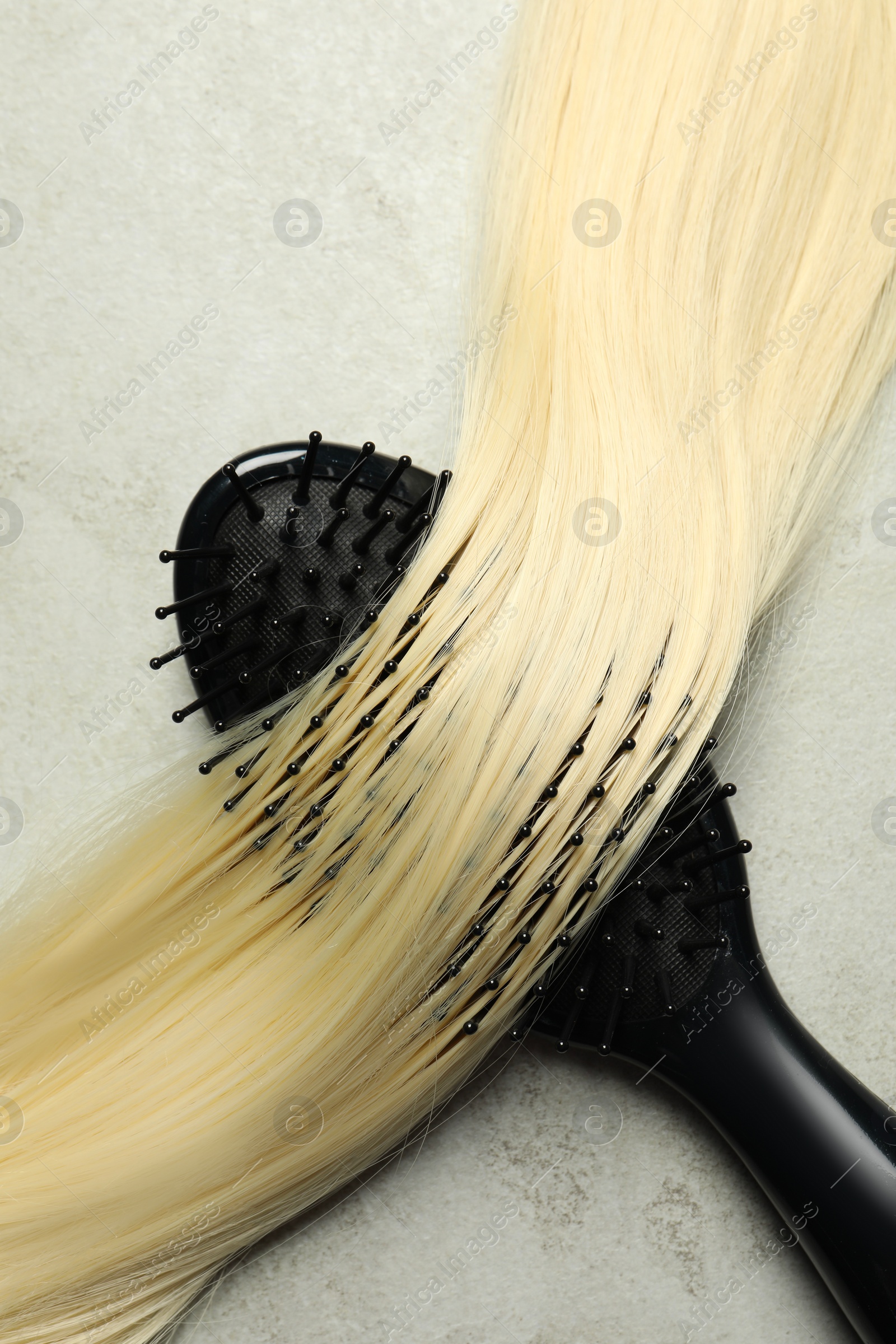 Photo of Stylish brush with blonde hair strand on grey table, top view