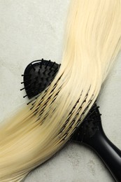 Stylish brush with blonde hair strand on grey table, top view