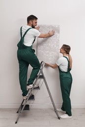 Photo of Workers hanging stylish wall paper sheet indoors