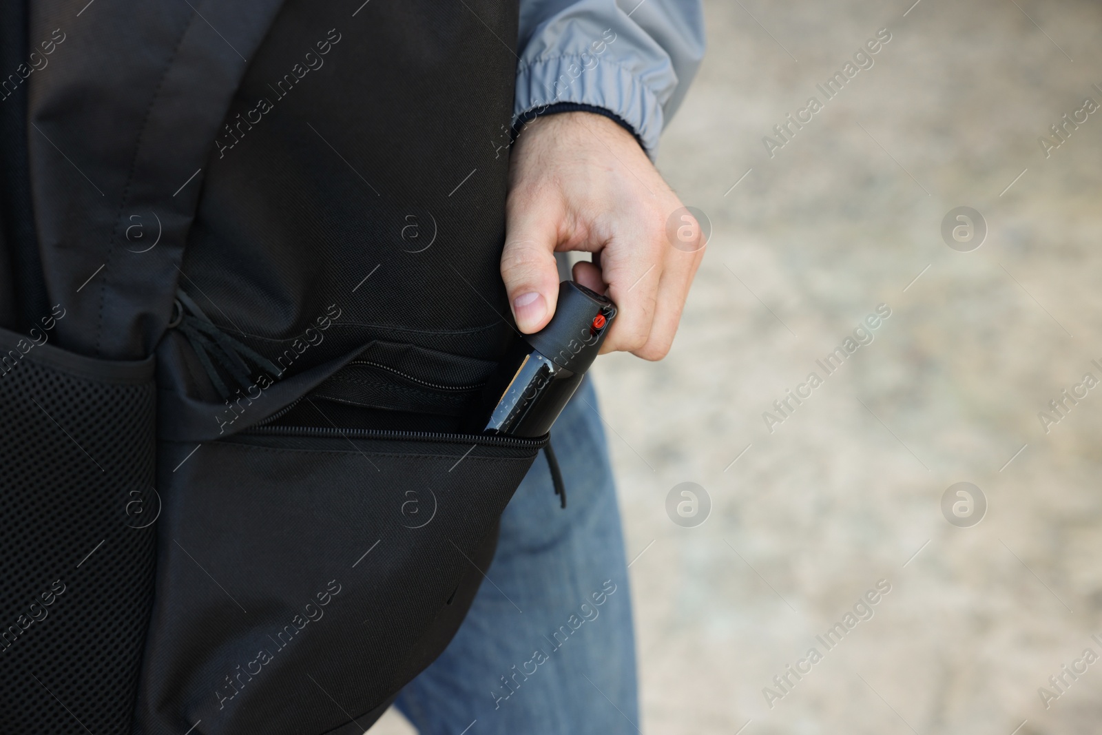 Photo of Man putting pepper spray into backpack outdoors, closeup. Space for text