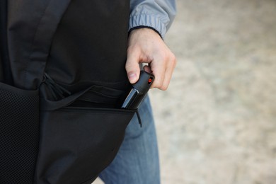 Man putting pepper spray into backpack outdoors, closeup. Space for text