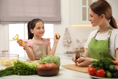 Mother and daughter peeling vegetables at table in kitchen