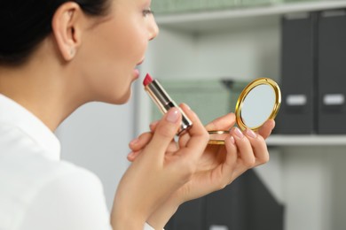 Young woman using cosmetic pocket mirror while applying make up indoors, closeup