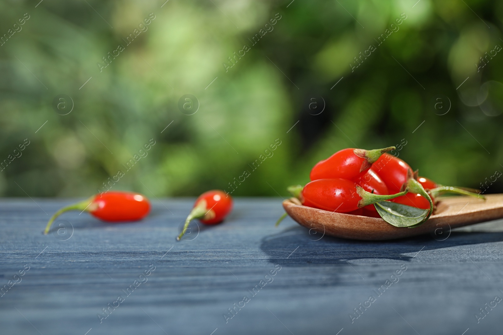 Photo of Spoon with fresh goji berries on blue wooden table against blurred background. Space for text