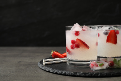 Glasses of refreshing drink with ice cubes and berries on grey table. Space for text