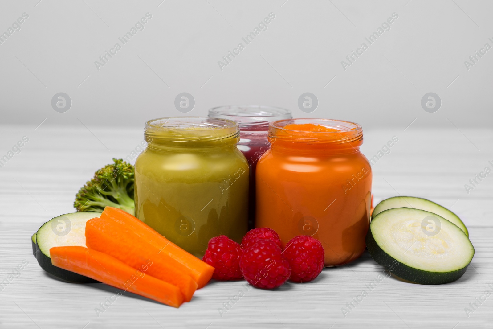 Photo of Jars with healthy baby food and ingredients on white wooden table