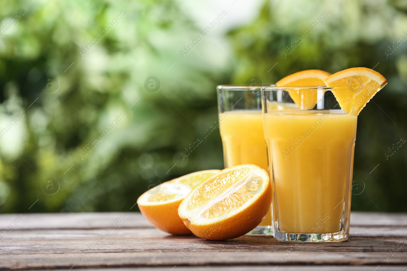 Photo of Glasses of orange juice and fresh fruit on wooden table. Space for text