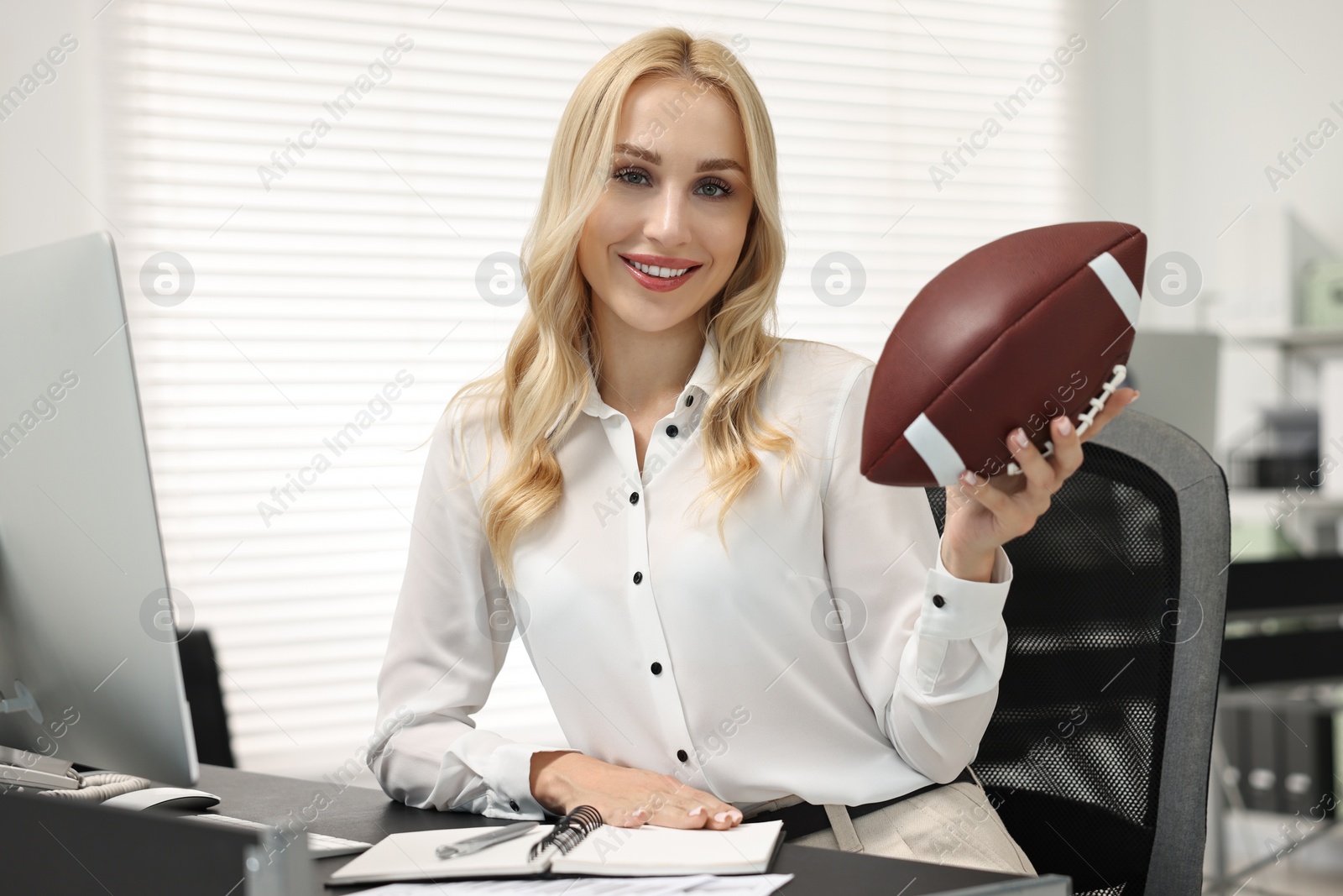 Photo of Happy woman with american football ball at table in office