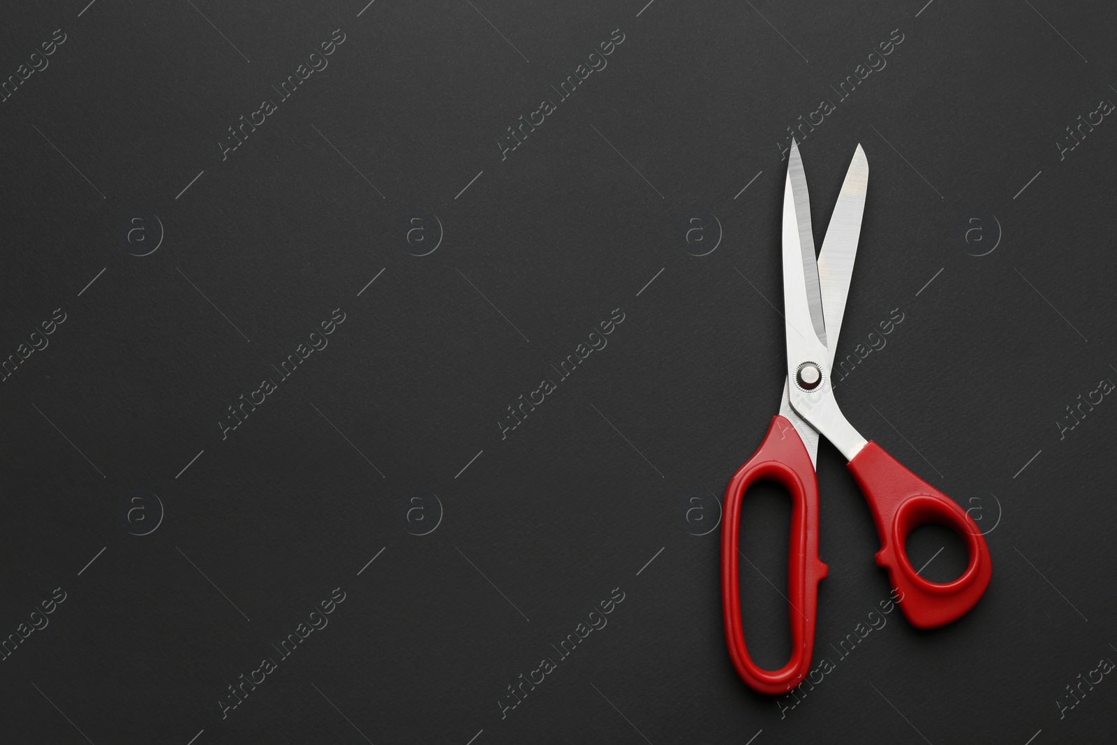 Photo of Pair of sharp scissors on dark background, top view. Space for text