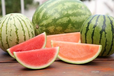 Different cut and whole ripe watermelons on wooden table outdoors