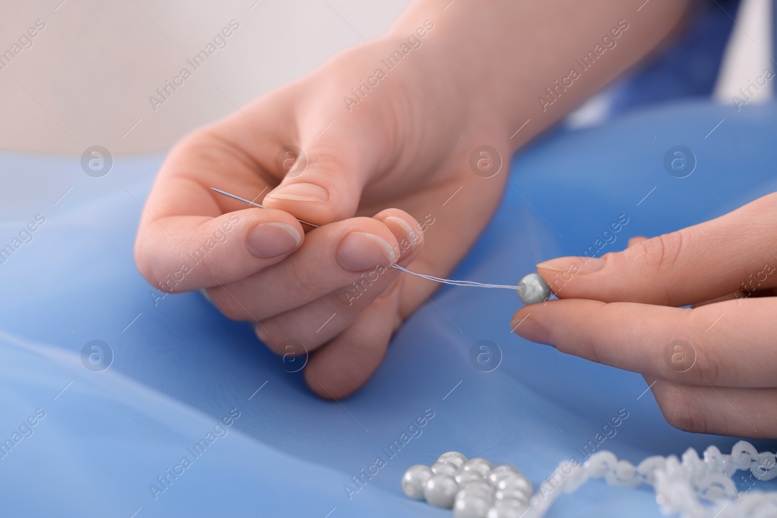 Photo of Dressmaker stringing bead on thread at light blue fabric in atelier, closeup