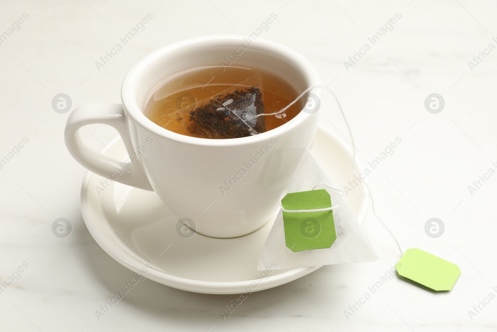 Photo of Tea bag in cup on white table, closeup