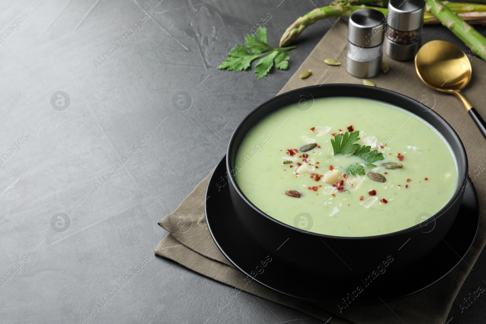 Photo of Bowl of delicious asparagus soup on dark table, space for text