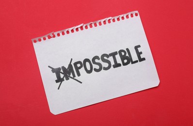 Photo of Motivation concept. Paper with changed word from Impossible into Possible by crossing over letters I and M on red background, top view