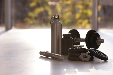 Photo of Adjustable dumbbells with bottle and jar of protein on floor indoors. Space for text