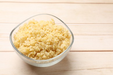 Photo of Delicious bulgur in glass bowl on wooden table, closeup. Space for text