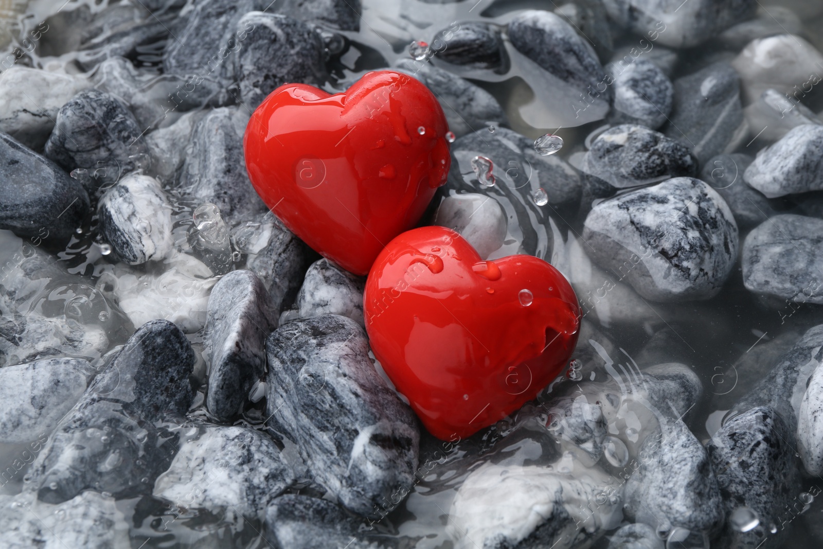 Photo of Red decorative hearts on stones and water