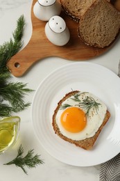 Plate with tasty fried egg, slice of bread and dill on white marble table, flat lay