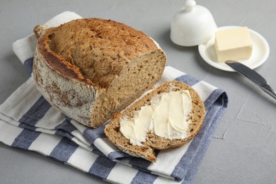 Slice of tasty bread with butter near loaf on grey table