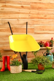 Photo of Wheelbarrow with gardening tools and flowers near wooden wall