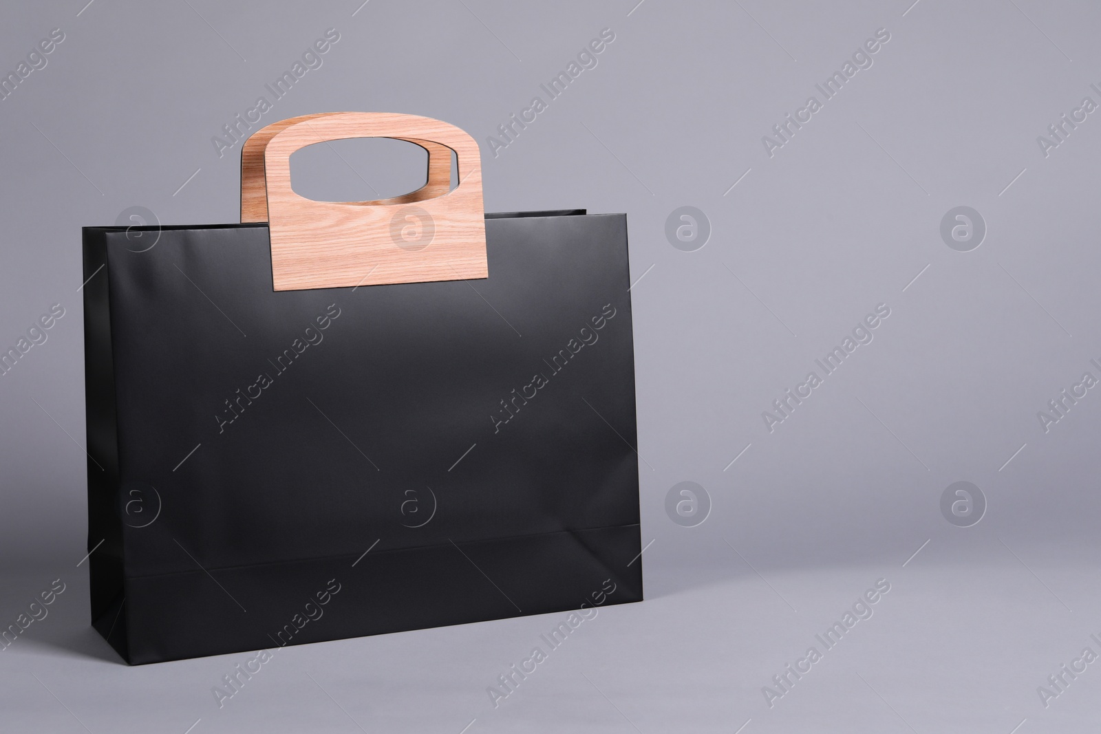 Photo of One black paper shopping bag on grey background. Space for text