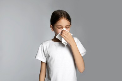 Photo of Little girl blowing nose into paper tissue on light grey background. Seasonal allergy
