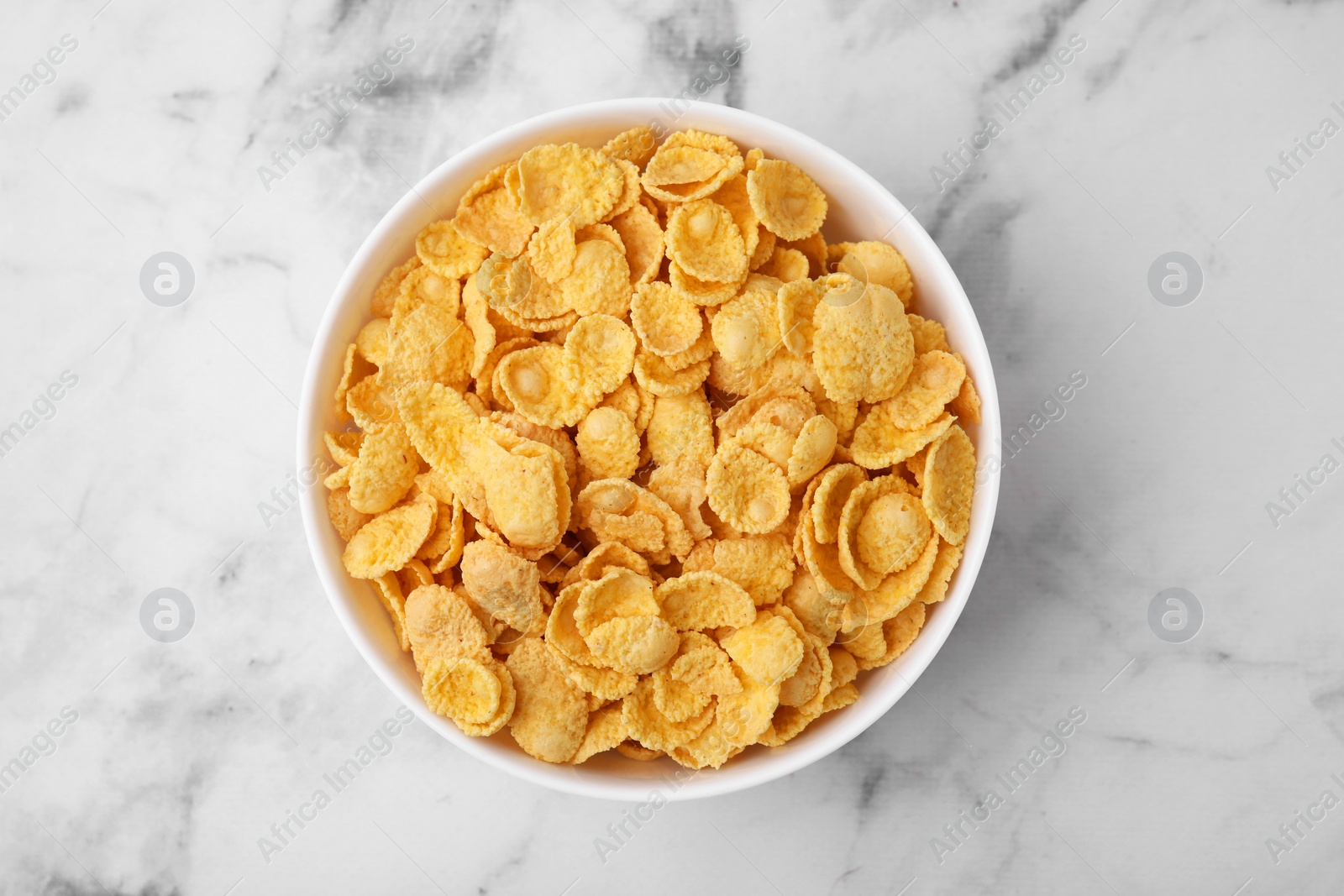 Photo of Tasty crispy corn flakes in bowl on white marble table, top view. Breakfast cereal