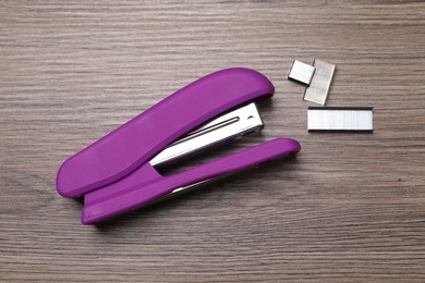 Photo of Purple stapler and staples on wooden table, top view