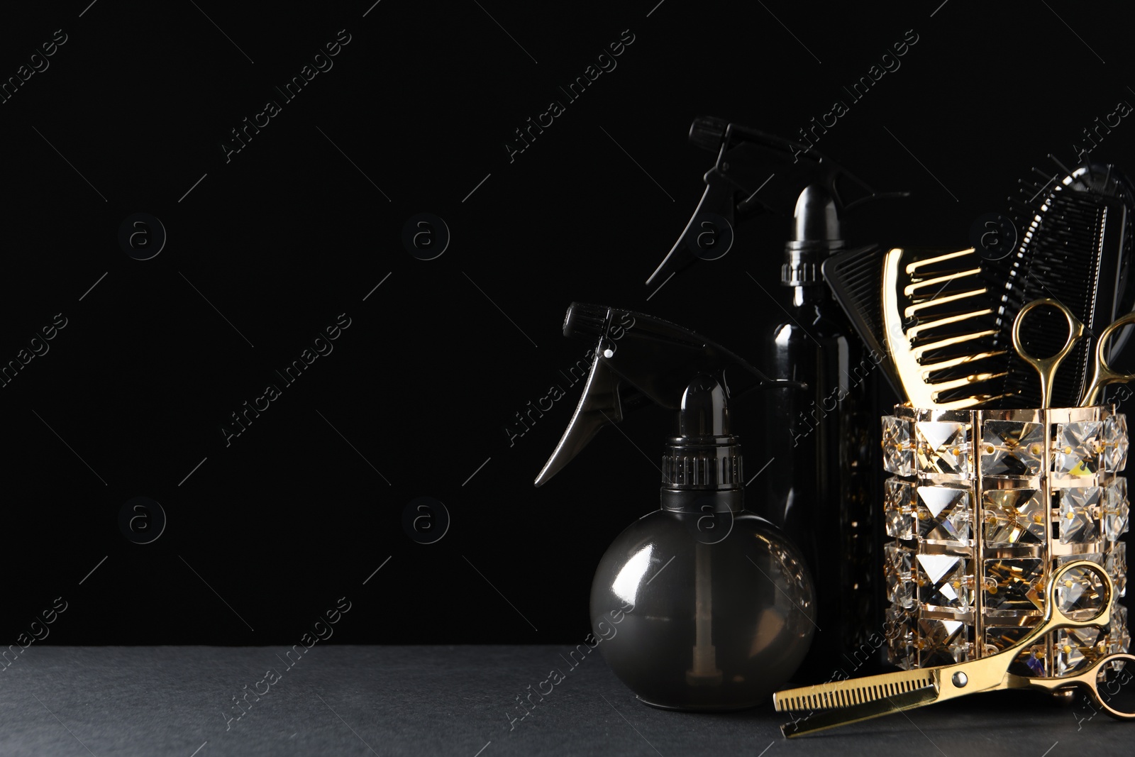 Photo of Different hairdresser tools on grey table against black background. Space for text