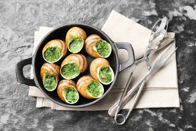 Photo of Delicious cooked snails in baking dish served on grey textured table, flat lay