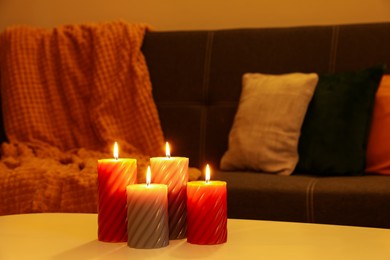 Photo of Beautiful candles on white table near sofa indoors. Cosy atmosphere