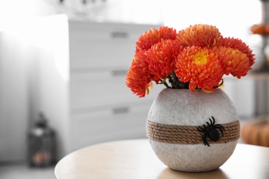 Photo of Beautiful flowers in vase with toy spider on table. Halloween interior decor