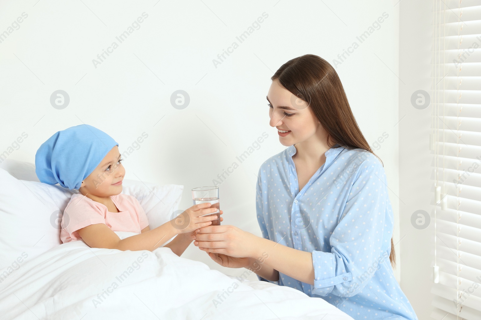Photo of Childhood cancer. Mother giving daughter glass of water in hospital