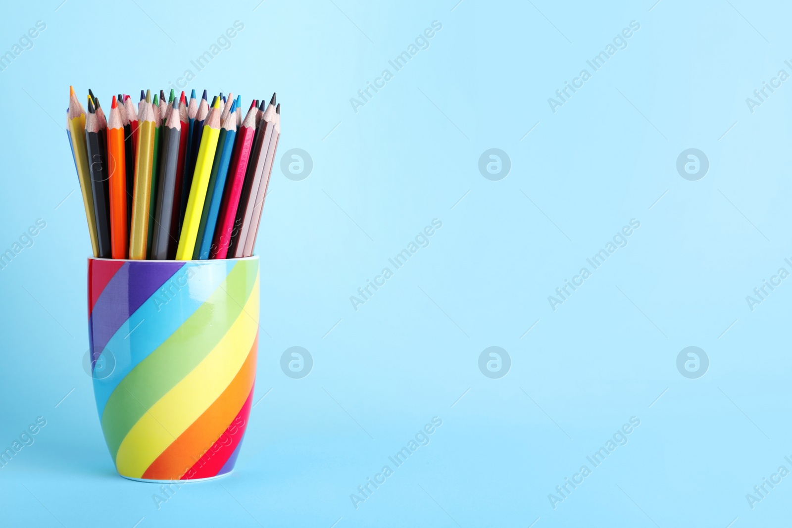 Photo of Colorful pencils in cup on light blue background. Space for text