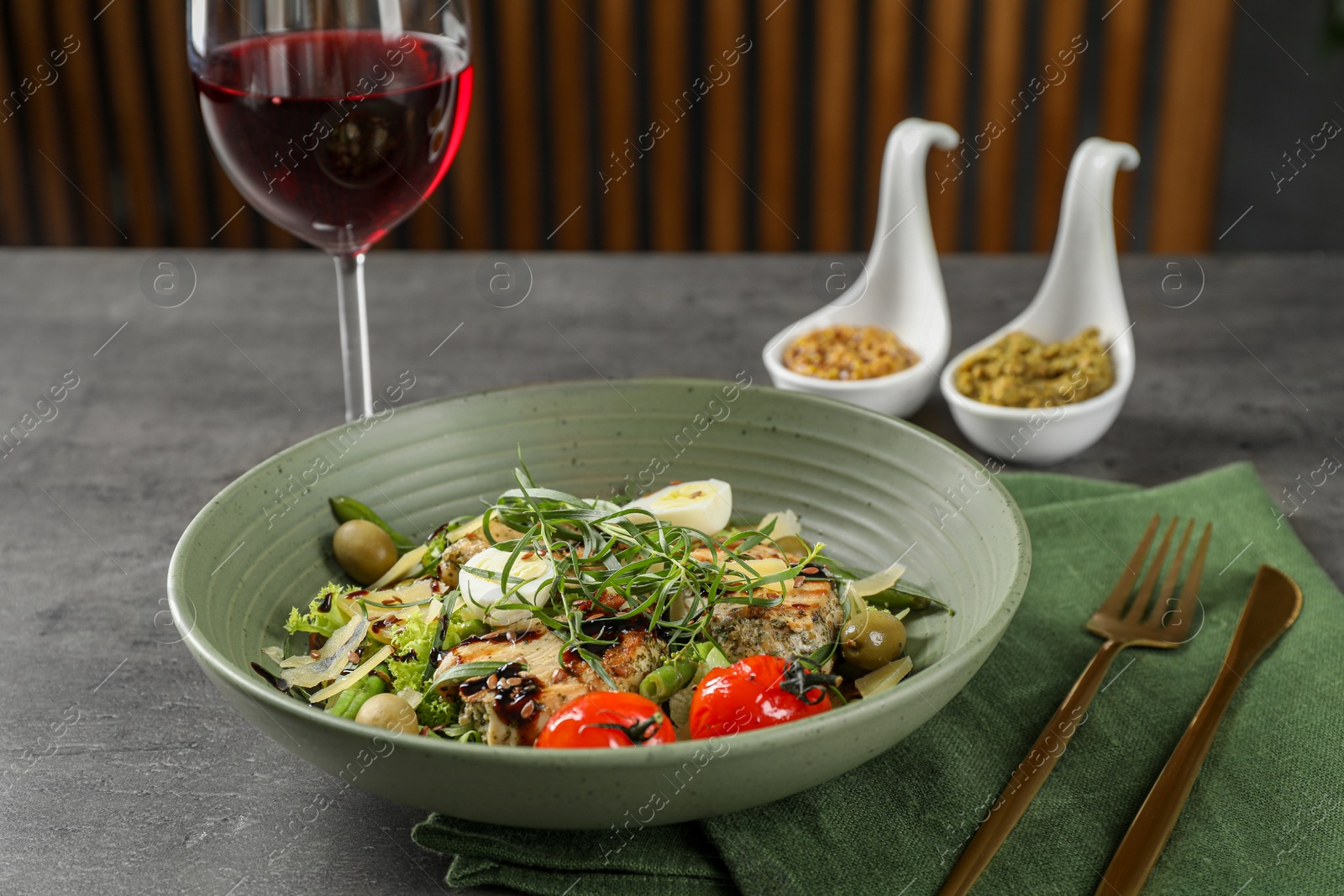 Photo of Tasty dish with tarragon, salad dressings and glass of wine served on grey table