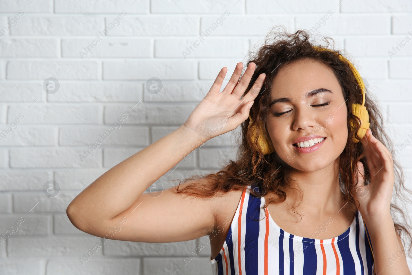 Photo of African-American  woman listening to music with headphones near brick wall