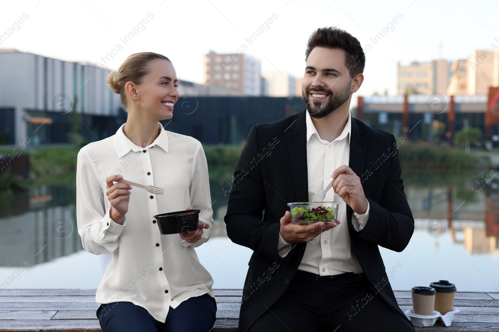 Photo of Smiling business people eating from lunch boxes outdoors