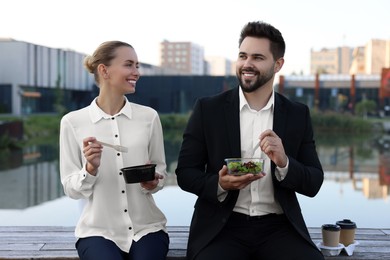 Smiling business people eating from lunch boxes outdoors