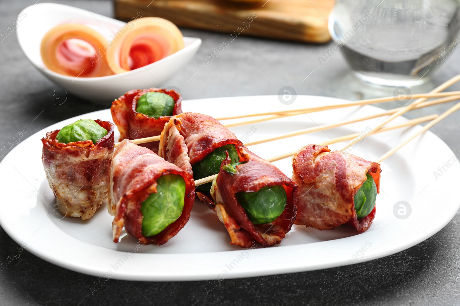 Photo of Plate with Brussels sprouts wrapped in bacon on grey table, closeup