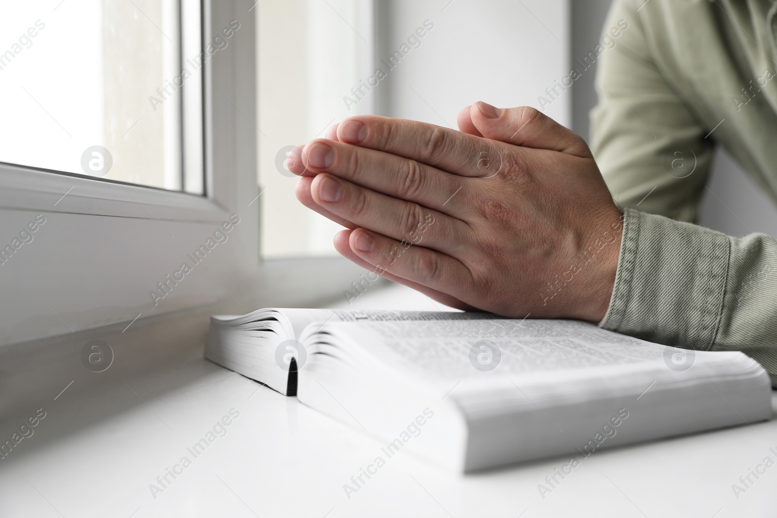 Photo of Religion. Christian man praying over Bible at windowsill, closeup