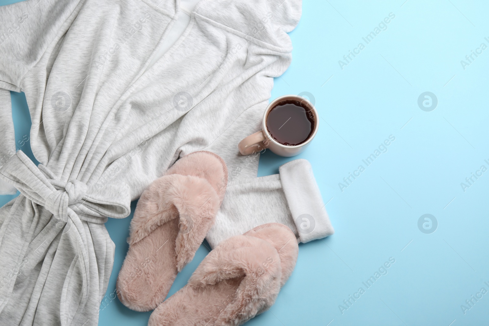 Photo of Fluffy slippers, robe and cup of coffee on light blue background, flat lay. Comfortable home outfit