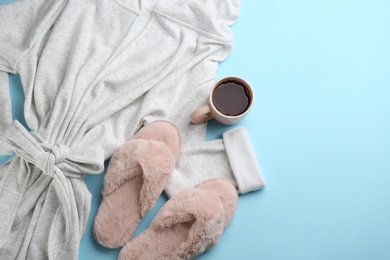 Fluffy slippers, robe and cup of coffee on light blue background, flat lay. Comfortable home outfit