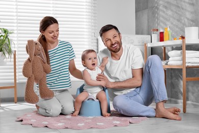 Parents training their child to sit on baby potty indoors