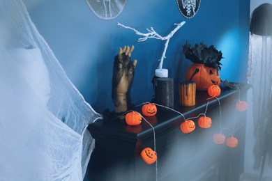 Photo of Jack-o'-lantern lights and different Halloween decorations on black fireplace near blue wall