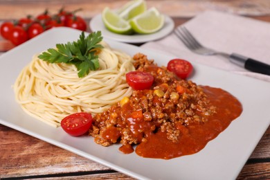 Tasty dish with fried minced meat, spaghetti, carrot, corn and cherry tomato served on wooden table, closeup