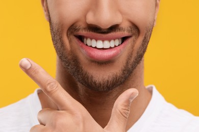 Photo of Smiling man with healthy clean teeth on orange background, closeup